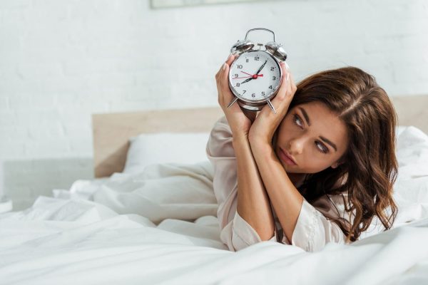 attractive woman holding alarm clock and lying in bed at morning